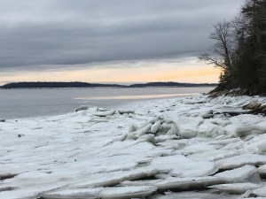 A sheet of broken ice on the ocean. The sky is dark gray until the horizon, which is gold with sunset.